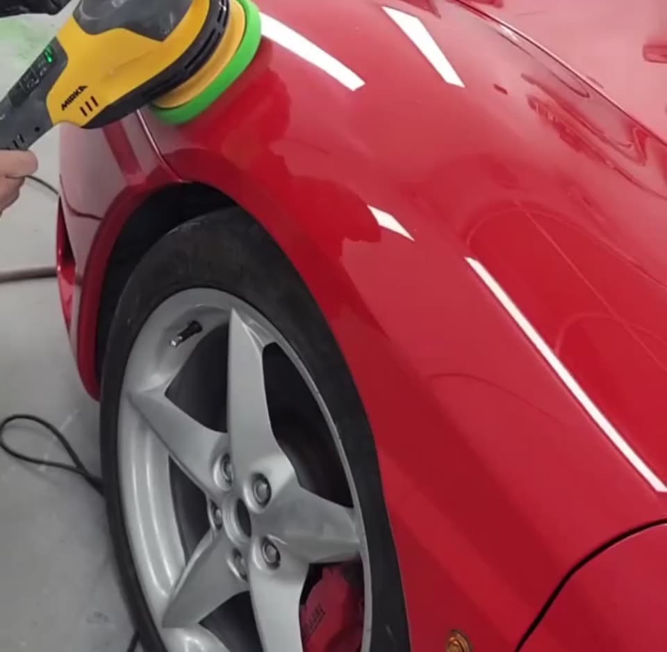 A technician machine polishing the front wing of a red car in the bay