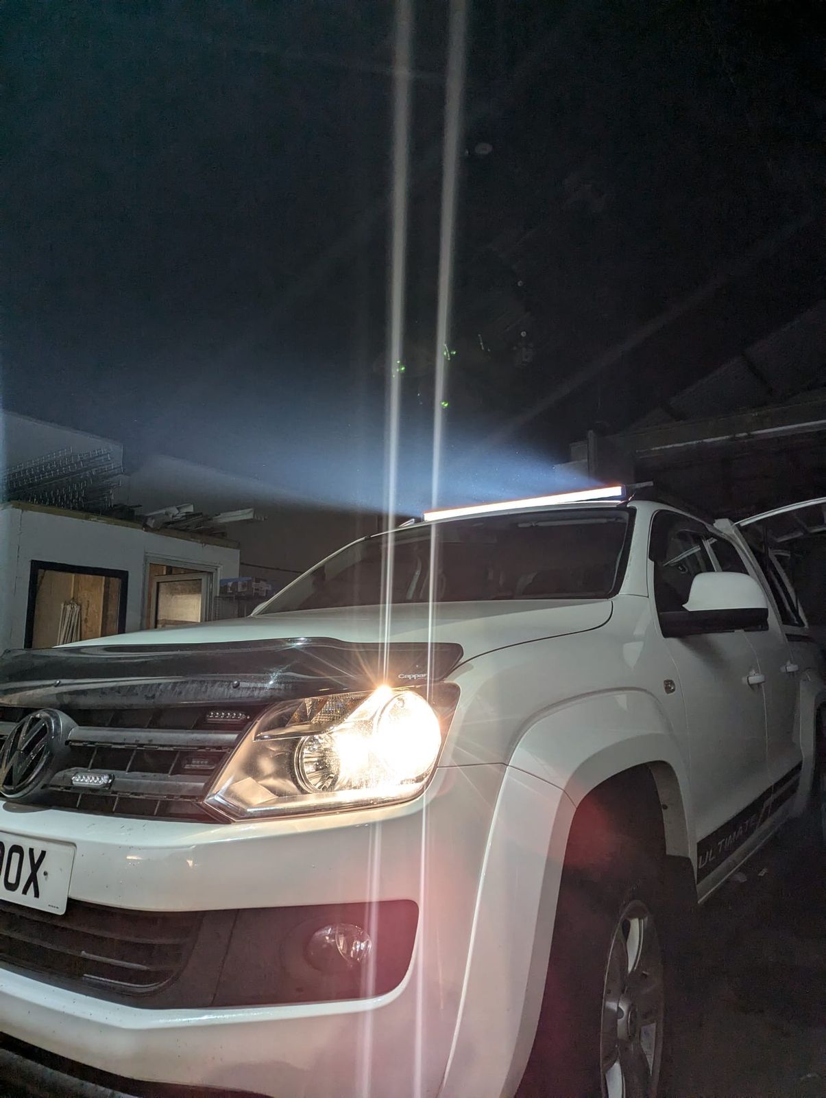 A white VW Amarok with a roof light bar lit in a dark workshop