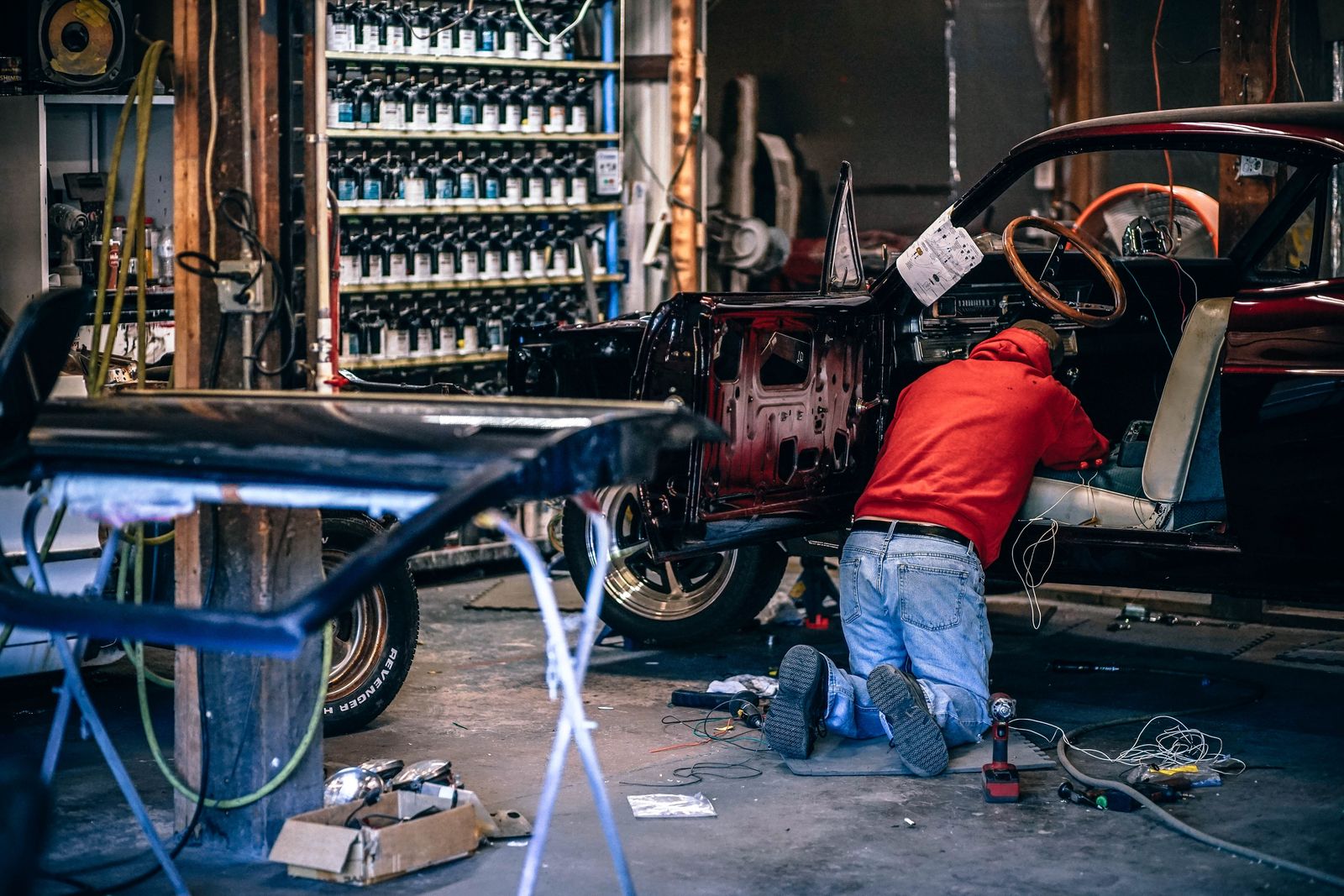 A technician working on a stripped door shell in a bodyshop, beside the paint mixing rack