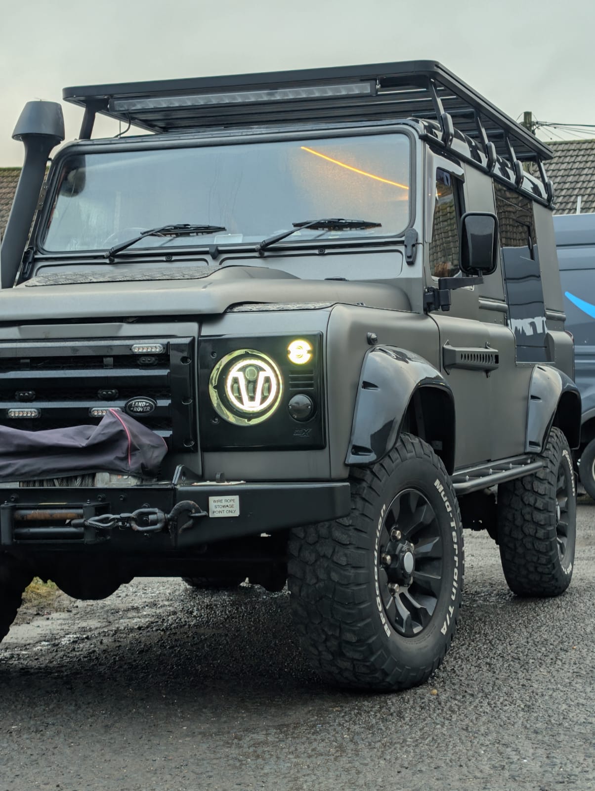 A matt black Land Rover Defender with a roof light bar, LED headlamps and a snorkel