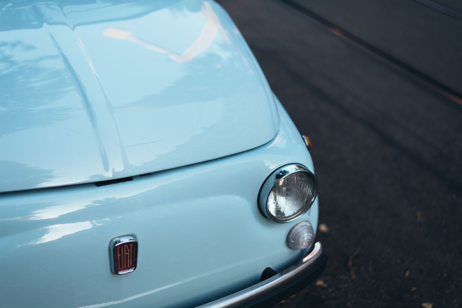 The headlamp and bonnet of a pale blue classic Fiat, close up