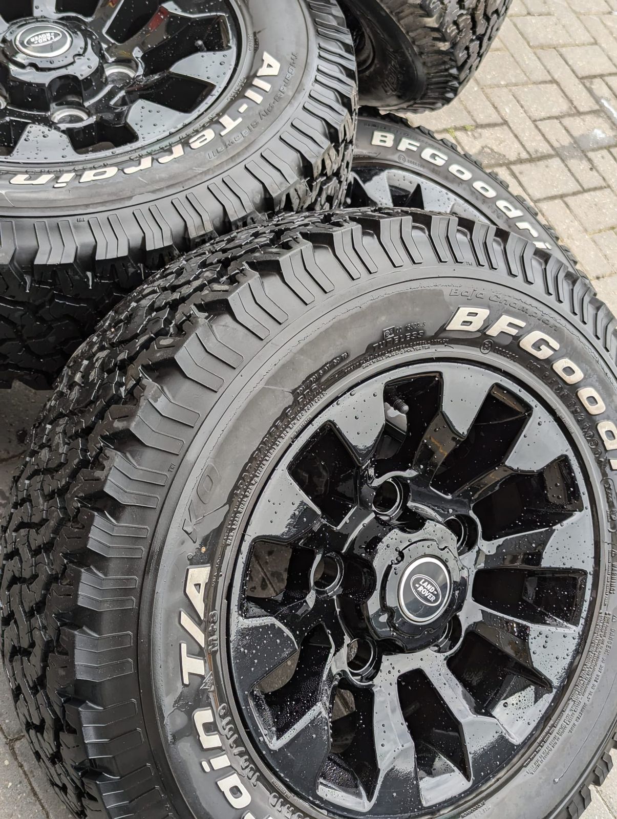 A stack of gloss black Land Rover alloys on all-terrain tyres, refinished at Rewind