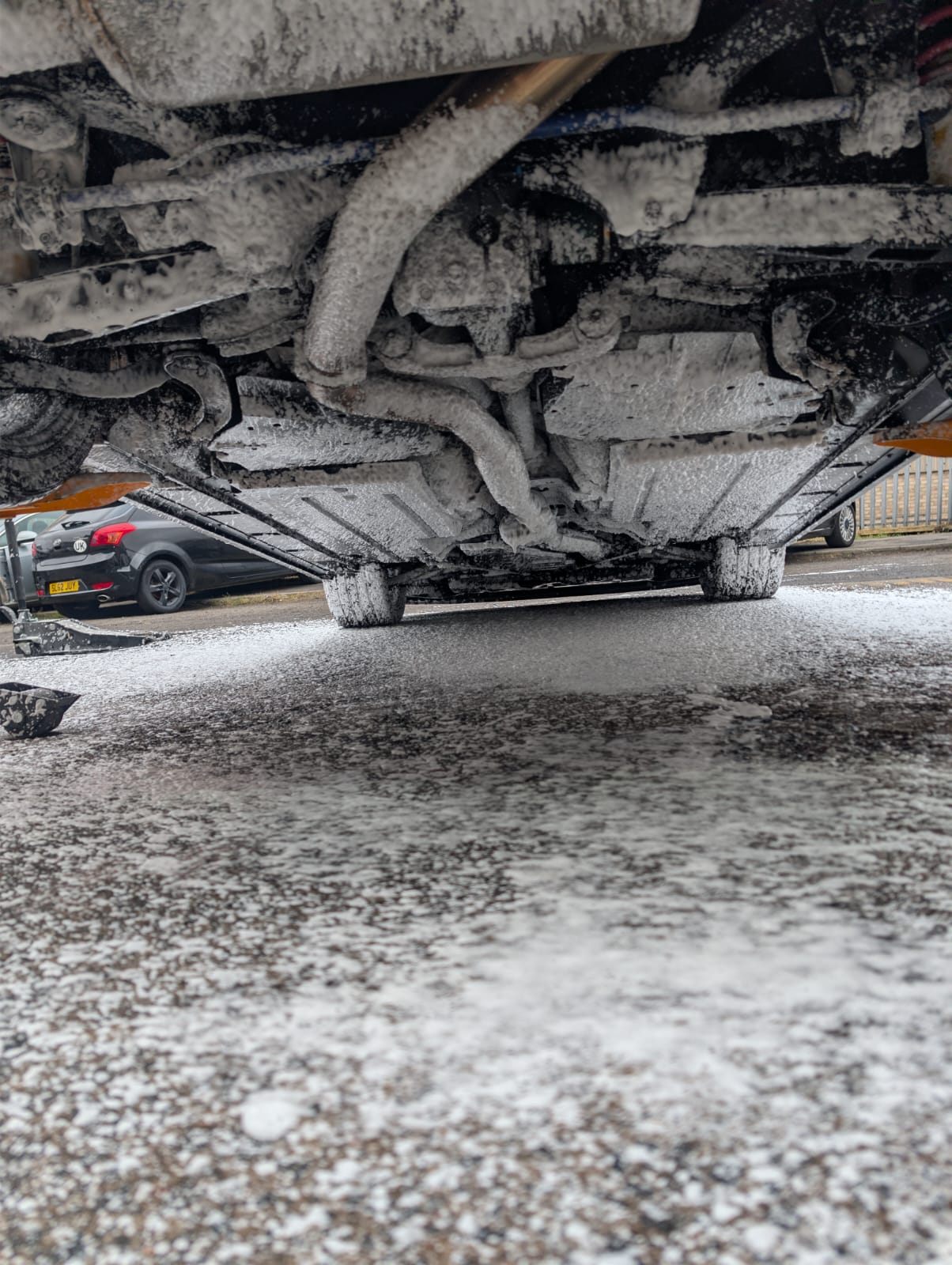 The underside of a car raised on the lift, foamed off before inspection